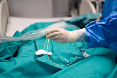 Ameliyat sırasında steril eldiven takan ve kateter tutan bir cerrah.