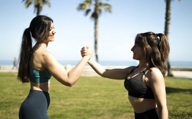 Sahilde başarılı bir antrenmanın ardından spor yapan iki bayan sporcu spor başarılarını kutluyor.