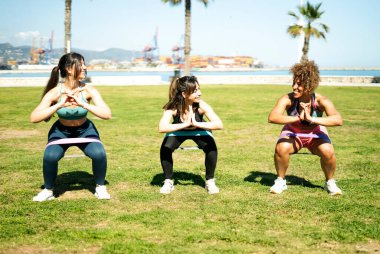 Parktaki spor salonunda direniş bantlarıyla çömelmiş üç kadın.
