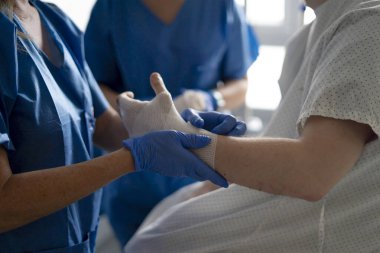 Tıbbi uzman bir hastanın elini sargılar ve tedavi eder, yaralarını iyileştirir ve ona destek olur.