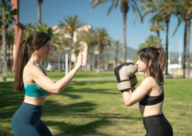 Parkta palmiye ağaçlarıyla boks antrenmanı yapan iki genç kadın.