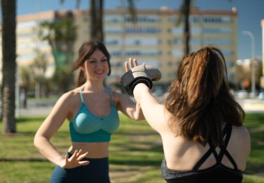 İki bayan arkadaş parkta boks antrenmanı yapıyor, boks eldivenleriyle birbirlerine beşlik çakıyorlar.