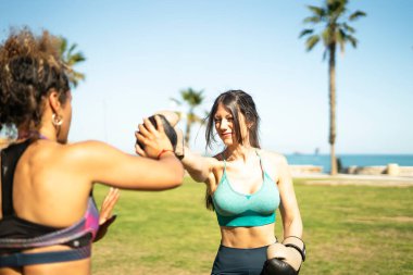 Deniz kenarındaki bir parkta boks antrenmanı yapan iki bayan sporcu.
