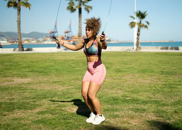 Deniz kenarındaki bir parkta atlama ipiyle atlama eğitimi alan sporcu kadın, sağlıklı yaşam tarzının tadını çıkarıyor.