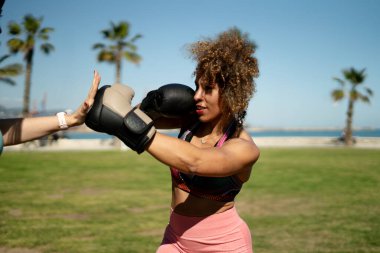 Deniz kenarındaki bir parkta kişisel antrenörüyle boks antrenmanı yapan bir kadın.
