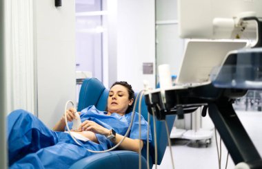 Ultrason cihazı kullanan kadın doktor, hastane yatağında yatan hastanın karnını muayene ediyor.