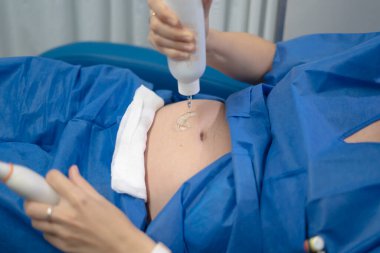 Doktor ultrason çevirici kullanıyor ve muayene sırasında hamile karnına vites jeli uyguluyor.