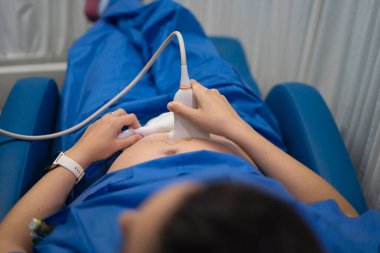 Doktor, hastanede yatan hamile bir kadının karnını muayene ederken ultrason tarayıcısı kullanıyor.