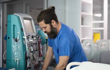 Bir hastane odasında hasta için diyaliz makinesi hazırlayan bir erkek doktor.