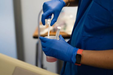 Mavi eldiven giyen hemşire küçük plastik bardakta ilaç ya da kimyasal solüsyon hazırlıyor.