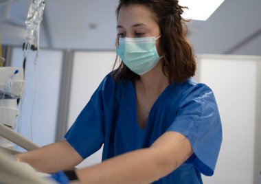 Ameliyat maskesi ve eldiven takan genç hemşire hastane odasında tıbbi malzemelerle çalışıyor.