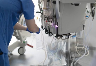 Sıvı yönetimi için şeffaf bir poşet bağlayan bir hastane odasında diyaliz makinesi çalıştıran bir tıp çalışanı.