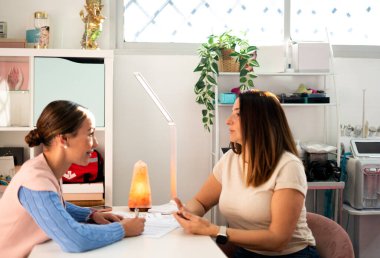 Güzellik uzmanı bir müşteriyle tedavi seçeneklerini tartışıyor, profesyonel güzellik salonu ortamında danışmanlık ve kişisel tavsiyelerde bulunuyor