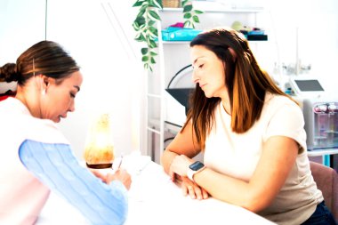 Güzellik uzmanı, güzellik salonunda müşteriyle görüşürken notlar alıyor.