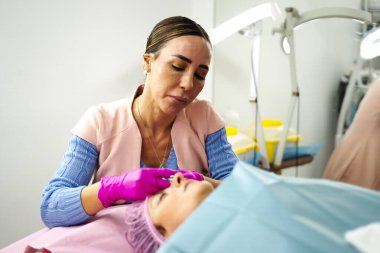 Profesyonel bir güzellik salonunda kozmetolog müşterinin kaşlarına mikropla tedavi uyguluyor.