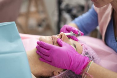 Dudak büyütme tedavisi için kadının dudaklarına hyaluronik asit enjekte eden pembe eldivenler giyen bir güzellik uzmanı.