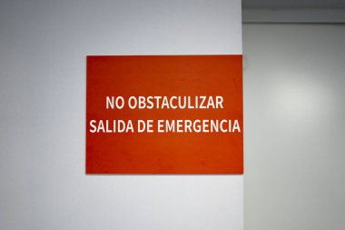 Parlak turuncu acil çıkış tabelasında İspanyolca kelimeler var. Engel yok, tükürük de aciliyet net bir rehberlik sağlıyor.