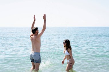 Çift yaz tatilinin tadını çıkarıyor, okyanusta su sıçratıyor.