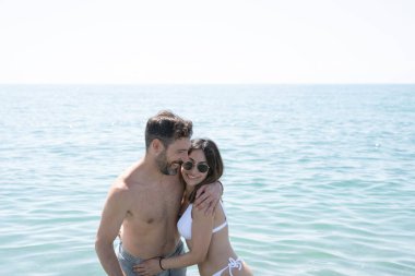 Romantik bir anın tadını çıkaran çift güneşli bir günde sakin okyanus sularında kucaklaşıp huzurlu ve huzurlu bir manzara yaratıyor.