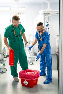 İki cerrah ameliyattan sonra tıbbi atıkları özel bir biyolojik tehlike konteynerine atıyorlar.