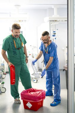İki cerrah ameliyat sonrası tıbbi atıkları özel bir konteynırda atıyorlar.