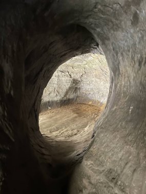 Kayaya oyulmuş doğal bir mağara gölgeli ve gizemli bir geçit sunuyor. Mağara duvarları ve tavanın kayalık ve düzensiz yüzeyleri loş iç dünya ile dış dünya arasında bir tezat oluşturuyor..