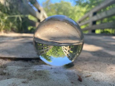 Crystal ball on wooden bridge inverts reality. Trees and sky reflect in the perfect symmetry, blurring the lines between earth and heavens. clipart