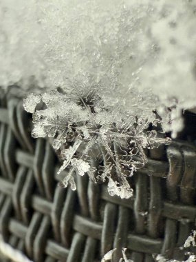 A crystalline snowflake perches delicately on woven fabric, its transparent arms reaching outward while dark textile patterns create dramatic contrast below. clipart