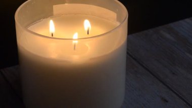 Mum alevleri zifiri karanlık zeminde dans ediyor, parlak ahşap masa yüzeyine altın yansımalar yansıtıyor, samimi bir ortam yaratıyor..