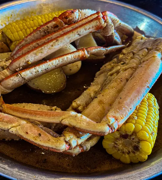 Buharlı sıcak yengeç bacakları metal tepside servis edilir. Koçanda mısır ve kırmızı patatesler, deniz ürünleri ziyafeti için aromalı Cajun yağı ile ıslatılır..