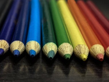 Keskinleştirilmiş renkli kalem uçlarını gökkuşağı sırasına göre dizin. Koyu mavi bir masa üzerinde yumuşak mavi bir arkaplan ile odaklanmış ön plan.