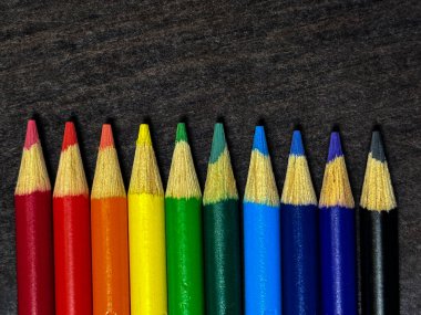Koyu renkli bir masa üzerinde gökkuşağı spektrumuna yerleştirilmiş bir sıra sivri renkli kalem. Kalem uçlarına odaklı temiz kompozisyon.