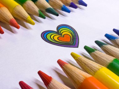 Kalp sembolü etrafında gökkuşağı sırasına dizilmiş renkli kalemler. Aşkı, LGBTQ + gururu, çeşitliliği, birliği ve dahil edilmeyi temsil eden sembolik ve yaratıcı konsept.