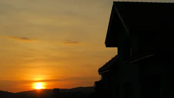 Dağlarda güzel bir günbatımına karşı bir evin silueti