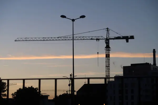 Gün batımında mor bir gökyüzüne karşı siluetli bir vinç ve inşaat yapıları.