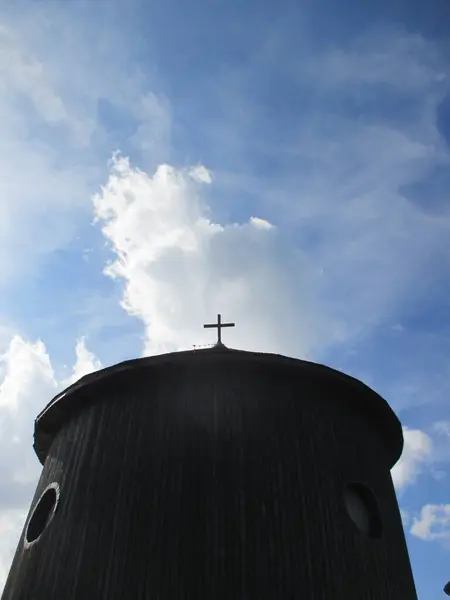 Mavi gökyüzüne karşı çatısında haç olan oval şekilli bir bina.