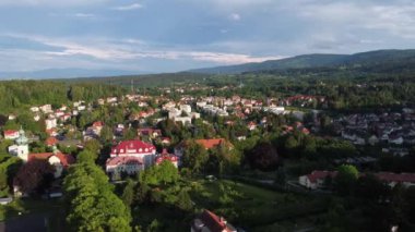 Uçan bir insansız hava aracı, dağların çarpıcı manzarasıyla bir turist kasabasının üzerinde uçuyor.