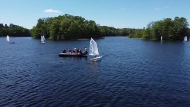 Bir İHA yaz tatilinde teknelerde dinlenen bir grup insana doğru bir gölün üzerinden uçuyor.
