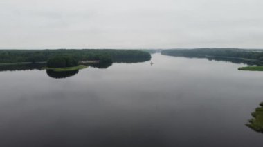Uçsuz bucaksız bir gölün üzerinde, sisli bir günde ormanı ve ufku gören yatay bir dron görüntüsü.