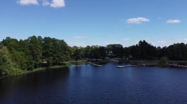 Yaz boyunca güzel bir orman, tekne ve yeşil bir kıyı şeridiyle gölün üzerinde uçan yatay bir dron görüntüsü.