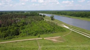 Yeşil tarlalar, ormanlar ve yaz boyunca nehir manzaralı bir tepede uçan bir dron görüntüsü.