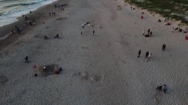 Gün batımında sahilde uçan bir dron, yürüyen turistleri yakalıyor.