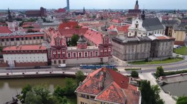 Nehir ve tramvay rayları boyunca eski ve güzel bir kasabanın üzerinde uçan panoramik bir dron görüntüsü.