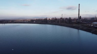 Bir fabrika ve binaların yakınındaki yapay bir gölün yüzeyinde uçan bir dron atışı.