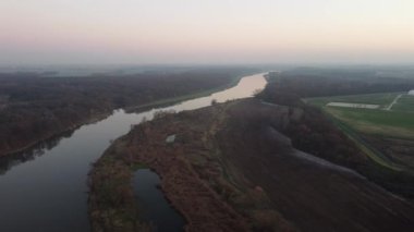 Sisli bir sonbahar akşamında ormanı ve nehri gören yatay bir insansız hava aracı.