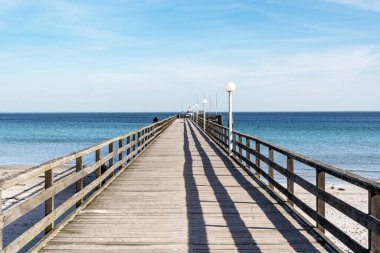 Almanya 'da Baltık Denizi' ne uzanan tahta kaldırımlı bir iskele. Gökyüzü mavi ve su sakin.