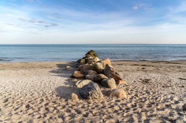 Üzerinde büyük bir kaya yığını olan bir plaj. Kayalar sahile saçılmış ve su sakin. Sahne huzurlu ve sakin, kayalar sahile bir denge hissi katıyor.