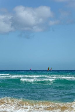 Fuerteventura İspanya 'da güzel mavi bir okyanus. Uzakta birkaç yelkenli var. Gökyüzü açık ve güneş parlıyor.