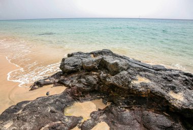 Fuerteventura İspanya 'da önünde büyük bir kaya olan kayalık bir plaj. Su sakin ve gökyüzü berrak.