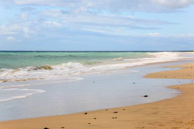 İspanya 'da Fuerteventura adalarında açık mavi gökyüzü ve birkaç bulutu olan bir sahil. Su sakin ve kum kuru.